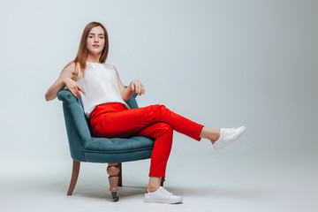 Fototapeta na wymiar Girl in red pants sitting in a chair on a light gray background
