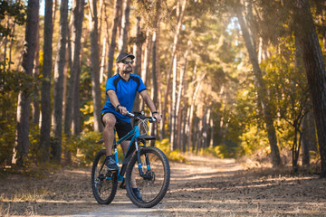 Fototapeta premium Happy bearded man cyclist rides in the sunny forest on a mountain bike. Adventure travel.