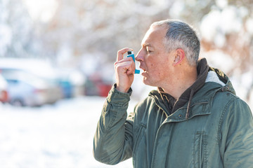 Mature man with inhaler having asthma attack outdoors.