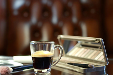 Cup of coffee with the phone and make-up set, shadow palette, and brushes