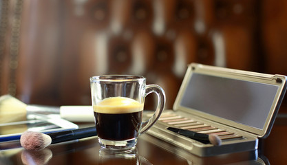 Cup of coffee with the phone and make-up set and brushes on the glass table