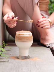 Woman hand holding a spoon full of cream and coco powder with a glass cup of coffee, milk, cream and coco powder.