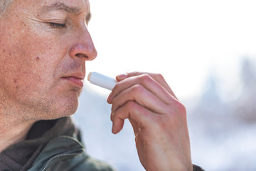 Handsome man applying balsam for lips, care of lips in the winter days.