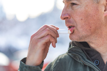 Handsome man applying balsam for lips, care of lips in the winter days.