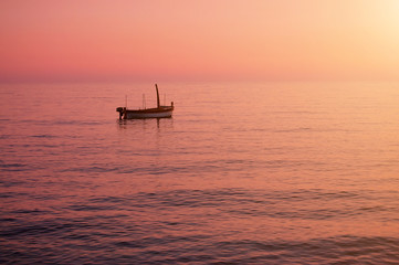 Small boat anchored in the calm sea in colorful sundown