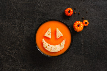 Pumpkin cream soup bowl for Halloween on the textured black table decorated with small pumpkins
