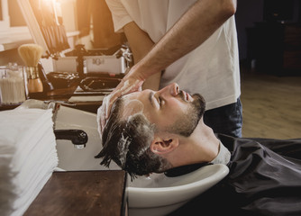 Young man with trendy haircut at barber shop. Barber washes customer head.