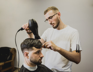 Young man with trendy haircut at barber shop. Barber does the hairstyle and beard trim.