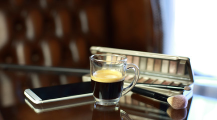 Cup of coffee with the phone and make-up set, shadow palette, and brushes