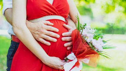 Pregnant woman in a red dress with her husband's hands