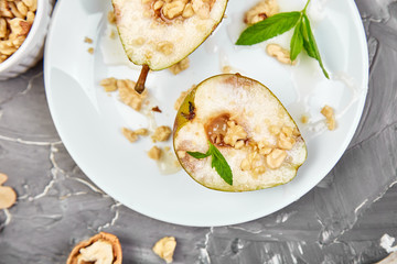 Tasty roast pears with honey and walnuts on white plates on grey background table. Top view.  Flat lay. Copy space.