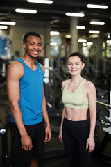 Fototapeta na wymiar Portrait of fit young couple smiling at camera while posing standing in modern gym, fitness coach concept