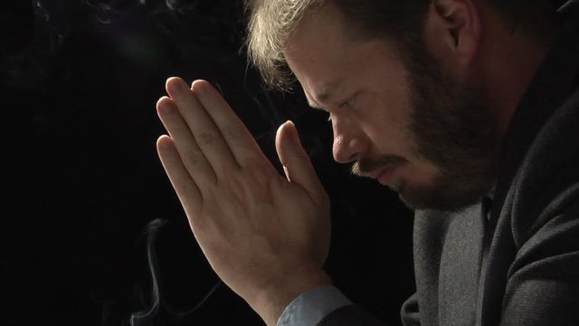 Close up profile shot of a business man in prayer. Backlit low key shot over black.