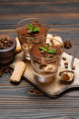Portion of Classic tiramisu dessert in a glass and savoiardi cookies on wooden background