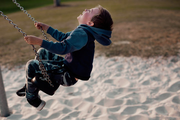 5 or 6 year old boy swinging on the swing at the playground, laughing