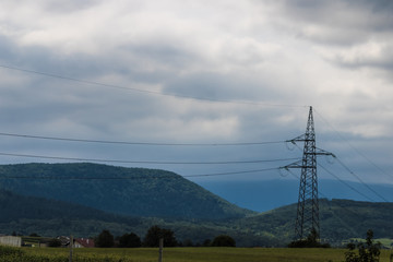Obraz premium High-voltage transmission line with the electricity tower, power line pole in the field with the mountain on background - Image