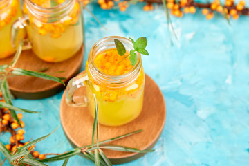 Colorful hot sea buckthorn tea with ginger and honey and sea buckthorn berries on blue table. Top view. Vitaminic healthy.