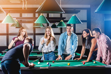Group of young cheerful friends playing billiards.