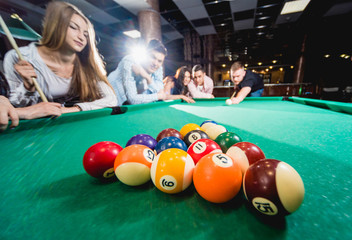 Group of young cheerful friends playing billiards.