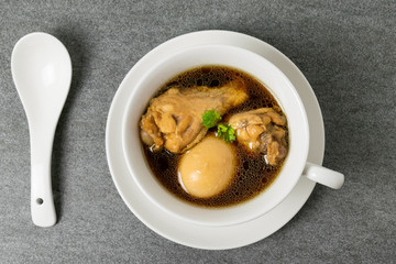 Hard-boiled eggs and chicken in sweet gravy soup in white bowl on tile table.