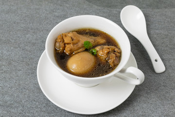 Hard-boiled eggs and chicken in sweet gravy soup in white bowl on tile table.