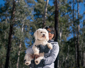 woman holding white dog in forest