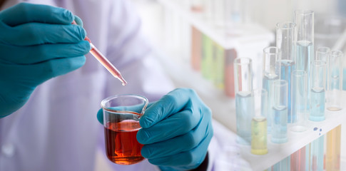 Laboratory research concept; scientist dropping chemical reagent into beaker with lab glassware background. Research in chemical laboratory.