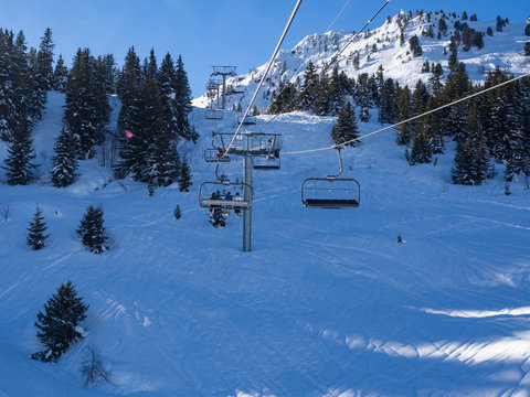 France, february 2019: Panoramic view of a snow covered alpine mountain range with chairlift ski lift in sun. Alpes