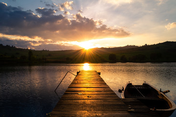 Sunset over a lake with a boat tied to a wooden pontoon 