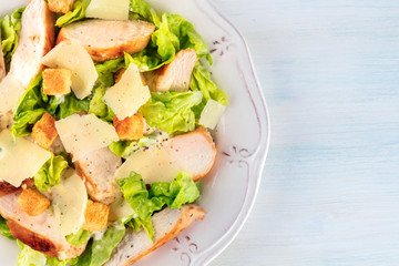 Caesar salad close-up. Slices of chicken breast, green lettuce, Parmesan cheese, and croutons, shot from the top with the typical dressing, with a place for text