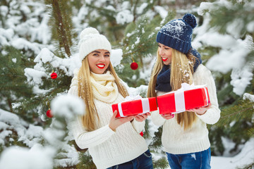 Girlfriends having fun with Christmas presents outdoors. Women holding gifts. Ladies holding red boxes on winter background