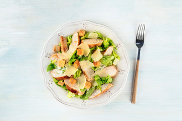 Chicken Caesar salad, shot from above. Slices of chicken breast, green lettuce, Parmesan cheese, and croutons with the typical dressing