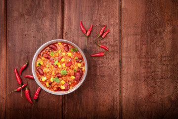 Chili con carne, a Mexican stew with red beans, meat, and chili peppers, shot from the top on a dark rustic wooden background with a place for text
