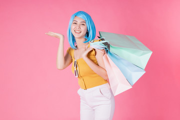 Pretty excited asian girl with colorful shopping bags showing  isolated over pink background .Asian shopaholic woman carrying shopping bags in colorful for summer sale concept .young blue hair girl .