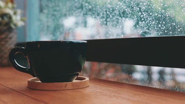 Hot coffee cup on table by the window in rainy day.