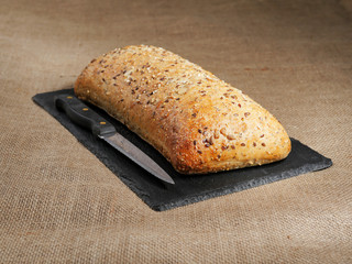 Uncut sourdough bread with nuts on a slate plate with a knife, Rustic hessian surface.