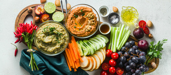 banner of veggie serving table with snacks with vegetables, fruits, baba ganoush and dip or spread of roasted red pepper and nuts. healthy vegan food for celebration or friends. shot from above. copy 