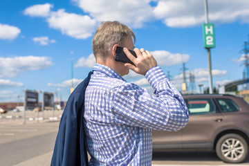 Middle-aged businessman in a blue suit calling by phone on the street parking