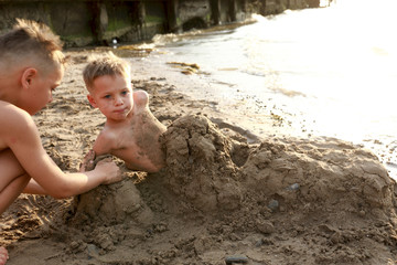 Boy burying his brother in sand