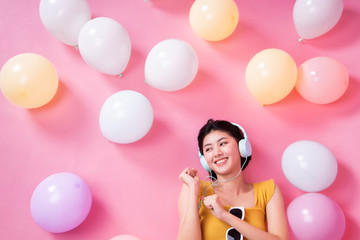 Fototapeta na wymiar Asian Beauty girl with colorful air balloons laughing over pink background. Young woman on birthday holiday party. Celebrating with pastel color balloon.She listen music and dance.