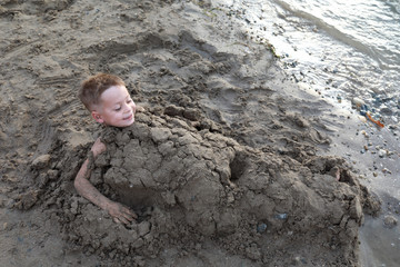 Happy boy buried in sand on beach