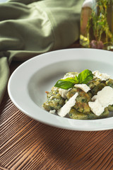 Green Gnocchi with basil, spinach, pesto feta cheese in composition with green cloth and olive oil. Close up, selective focus. Traditional italian cuisine. delish food photography, advertisment