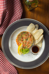 Fresh Salmon tartare, avocado with croutons and soy sauce in white plate on wooden background in composition with red cloth. Copy space. Top view