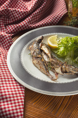 Close up Grilled fish with salad on white plate in composition with red cloth on wooden table. Food photo background. Seafood