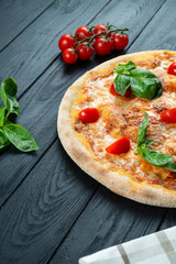 Homemade fresh Pizza Margherita with red sauce, basil and cherry tomato on a black wooden with copy space. Top view food photo. Flat lay. Italian cuisine.