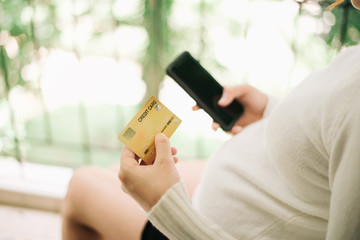 Pregnant woman holding a credit card and using mobile phone for online shopping, technology and people concept