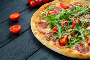 Homemade fresh Pizza with salami, cherry tomatoes and arugula on a black wooden with copy space. Top view food photo. Flat lay. Italian cuisine.