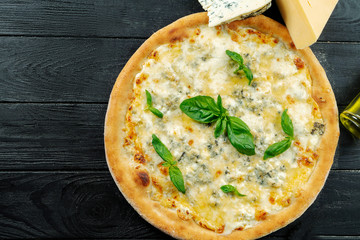 Homemade fresh Pizza with four cheese and basil on a black wooden with copy space. Top view food photo. Flat lay. Italian cuisine. Close up