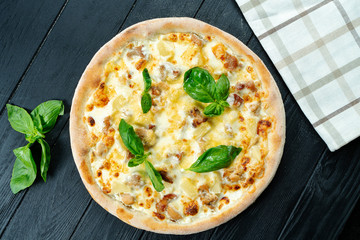 Homemade fresh Pizza with smoked chicken, mushrooms, basil and white sauce on a black wooden with copy space. Top view food photo. Flat lay. Italian cuisine.