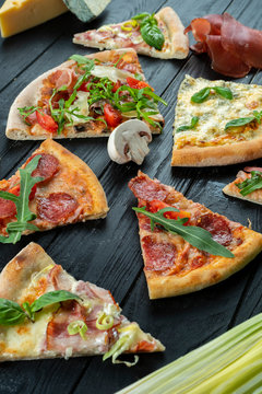 Different slices of pizza on dark wooden background. Italian cuisine. Food photo background. Food flat lay
